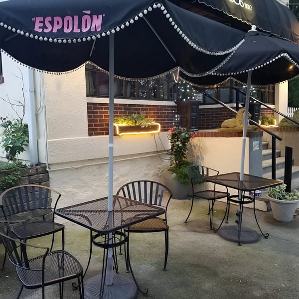 Outdoor patio of The 808 Bistro with black tables, chairs, and umbrellas, illuminated by string lights.
