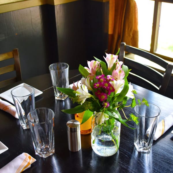 A set table at The 808 Bistro with glasses, napkins, and a vase of pink and white flowers.