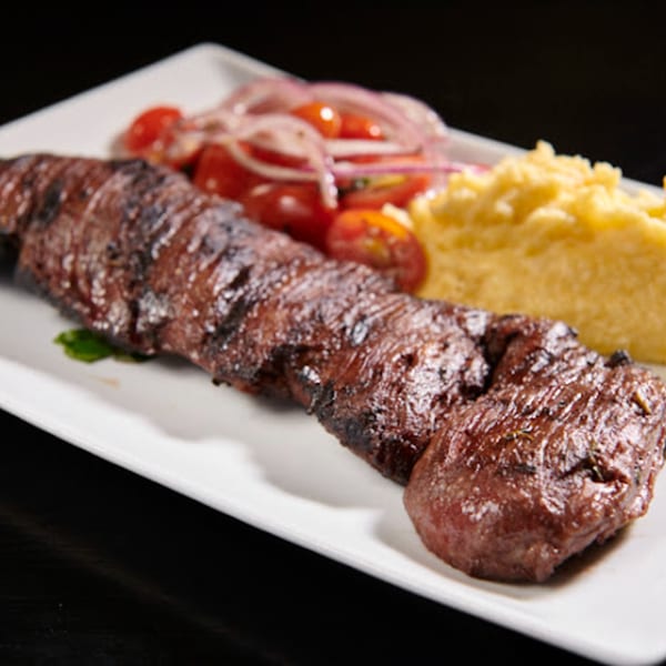 Grilled steak with a side of polenta and a tomato and red onion salad on a white plate.