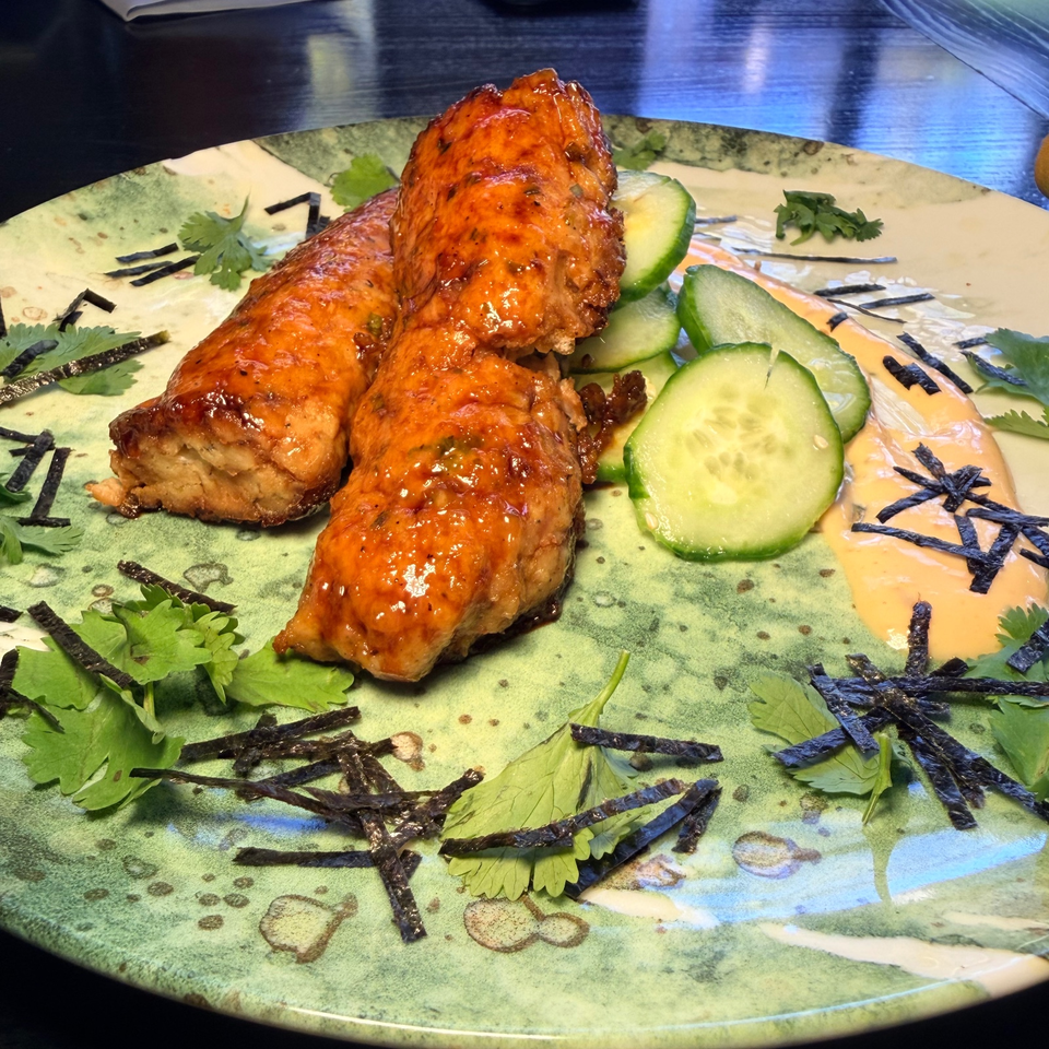 Three glazed, grilled chicken skewers served with cucumber slices, creamy sauce, cilantro, and shredded seaweed on a decorative plate.