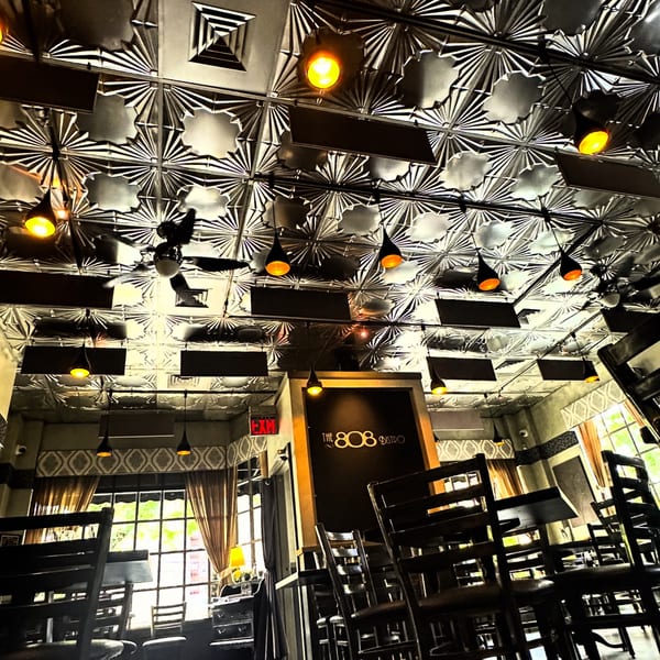 The 808 Bistro's dining room with a patterned ceiling, hanging lights, and wooden chairs.