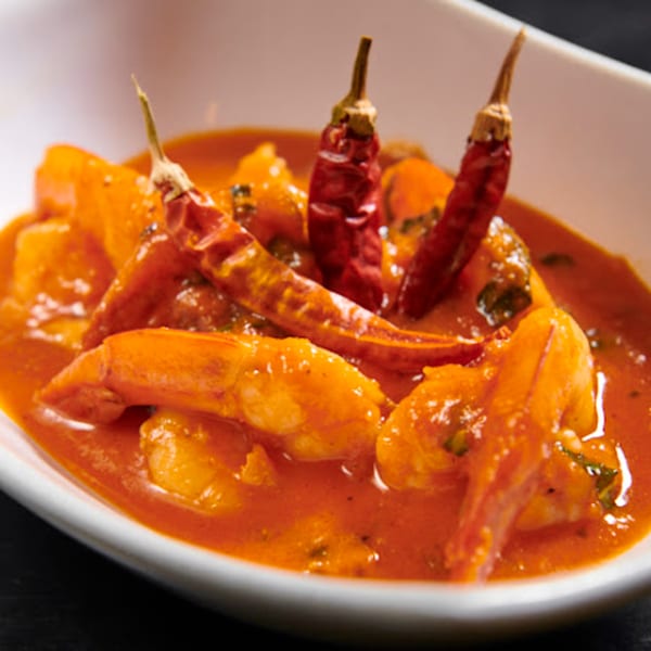 Shrimp and potatoes in a vibrant red sauce, garnished with three dried red chili peppers.