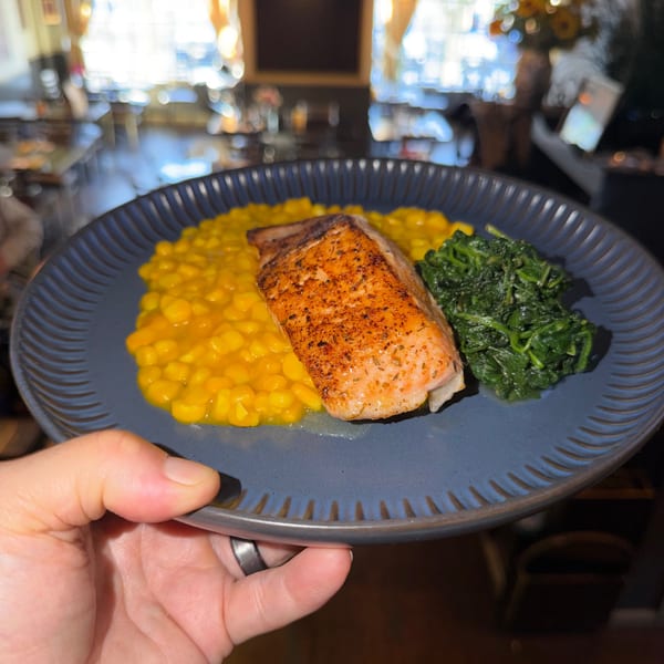 A hand holds a blue plate with salmon, yellow risotto, and green spinach at The 808 Bistro.