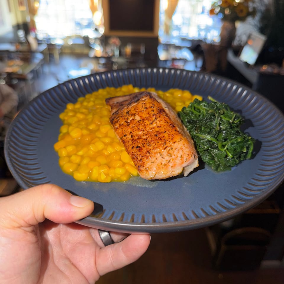 A hand holds a blue plate with salmon, yellow risotto, and green spinach at The 808 Bistro.