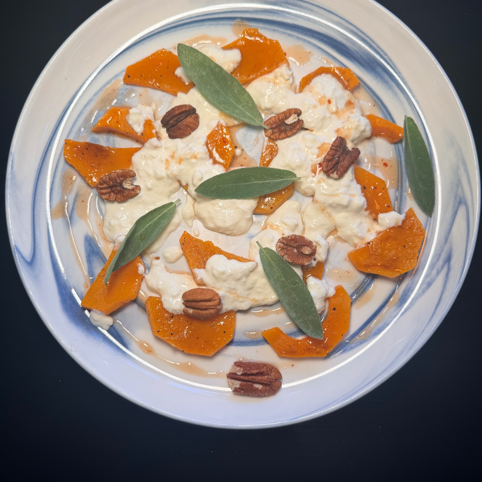 Creamy pasta with roasted squash, pecans, and fresh sage leaves arranged on a blue-rimmed plate.