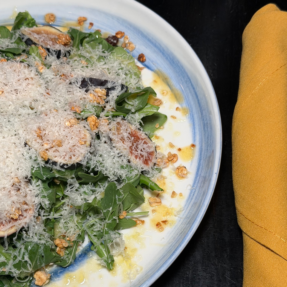 Leafy green salad topped with grated cheese, walnuts, sliced fruit, and dressing on a blue-rimmed plate beside a mustard napkin.