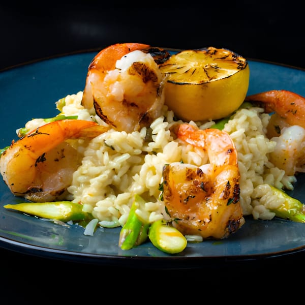 Grilled shrimp and asparagus risotto with a charred lemon half on a blue plate.