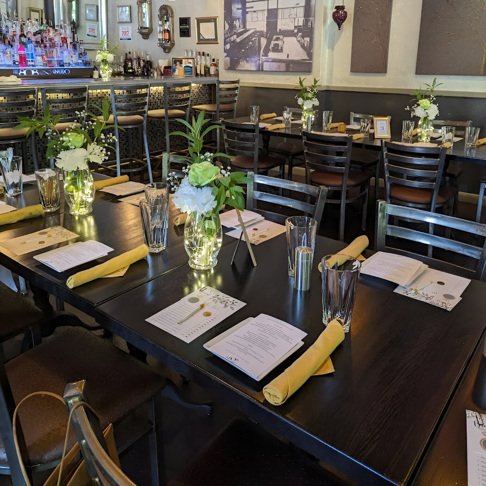 Set tables with menus, glasses, yellow napkins, and floral centerpieces in The 808 Bistro dining room.