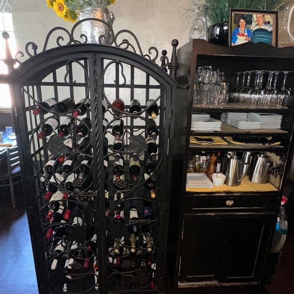 A black wrought iron wine rack filled with bottles next to a cabinet with glasses and plates.